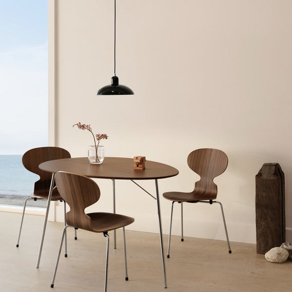 Modern round wooden table with three matching brown chairs, accented by a sleek black pendant light and neutral walls.