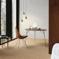 "Cozy brown chair and round wooden table against a textured beige floor and white brick wall, with soft gray pendant lights."