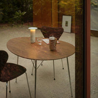 Round wooden table with a smooth finish, complemented by sleek metallic legs and dark patterned chairs.