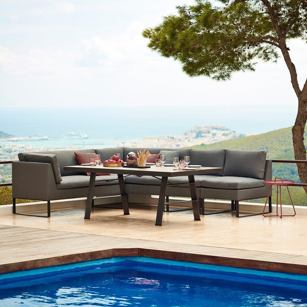 "Modern gray outdoor sectional sofa with sleek black legs, set against a serene blue pool and natural landscape."
