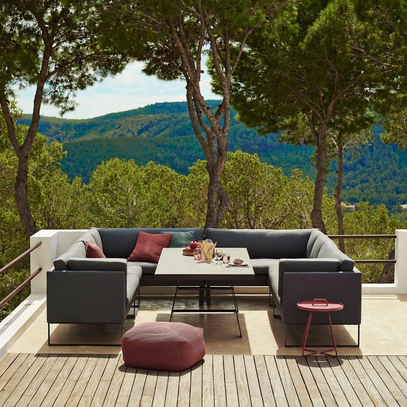 Modern outdoor sectional sofa featuring dark gray cushions, burgundy accents, and a neutral-tone tabletop.