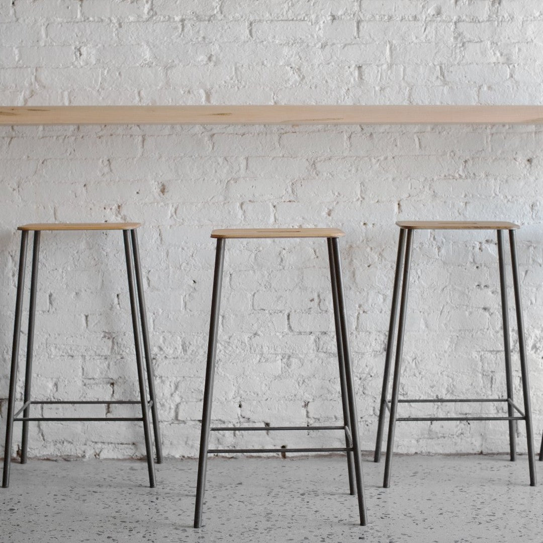 Set of three modern bar stools featuring natural wood seats and sleek black metal legs against a white brick wall.