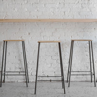 Set of three modern bar stools featuring natural wood seats and sleek black metal legs against a white brick wall.