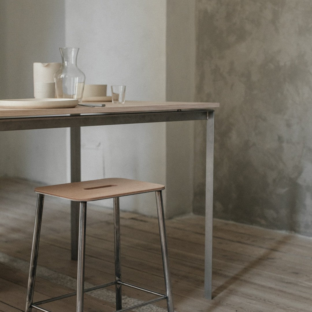 Natural wood table with a light beige top, sleek silver legs, paired with matching cream dinnerware and textured gray wall.