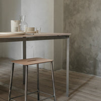 Natural wood table with a light beige top, sleek silver legs, paired with matching cream dinnerware and textured gray wall.