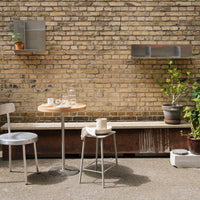 Gray metal furniture with natural wood accents against a textured brick wall, complemented by green plants in pots.