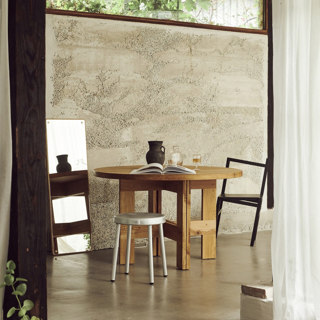 "Natural wood table with a light grey stool, complemented by a textured concrete wall and minimalist decor."