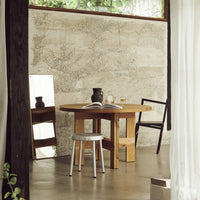 "Natural wood table with a light grey stool, complemented by a textured concrete wall and minimalist decor."