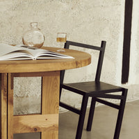 Natural wood table paired with a sleek black chair against a textured wall. Earthy tones and modern design elements.