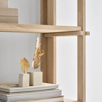 Light wood shelf with neutral-toned blocks and dried leaves against a minimalist white background.