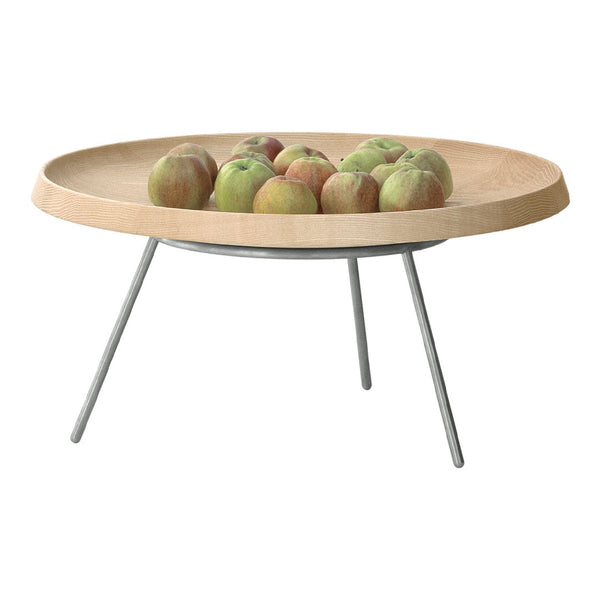 Light wood round serving tray with a smooth finish and silver metal legs, featuring green and red apples on top.