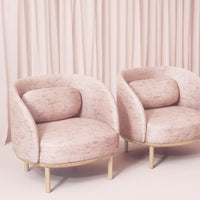 Soft pink armchairs with subtle textured pattern and gold legs, against a pastel curtain backdrop.