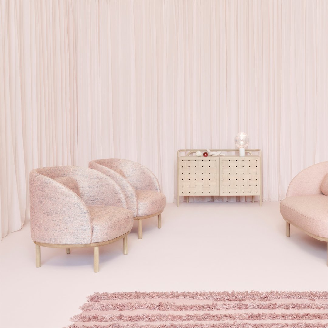 Soft pink armchairs and a light beige cabinet against a backdrop of blush drapes and a textured rug.
