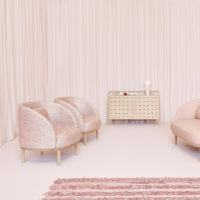 Soft pink armchairs and a light beige cabinet against a backdrop of blush drapes and a textured rug.