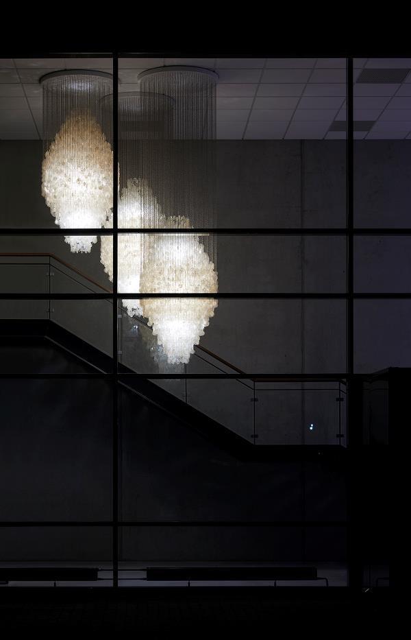 Elegant white chandelier with intricate patterns, glowing softly against a dark background. Modern lighting decor.