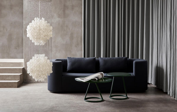 Navy blue sofa with textured cushions, green table, and soft white pendant lights against a neutral gray background.