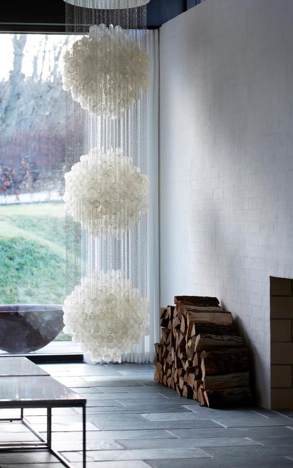 Three fluffy white pendant lights hang in a modern space, contrasting with the earthy tones of stacked wood and gray tiles.