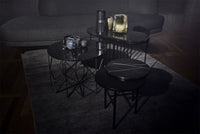 "Black geometric coffee tables with glossy surfaces on a dark gray rug, accentuated by soft shadows."