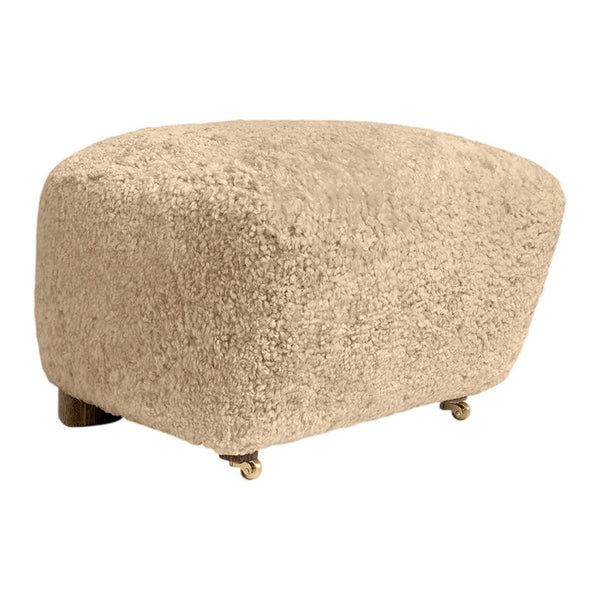 Beige upholstered ottoman with a soft, textured fabric and rounded shape, featuring gold wheels for mobility.