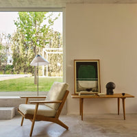 Beige fabric armchair with natural wood frame, paired with framed green artwork and sleek black decor accents.