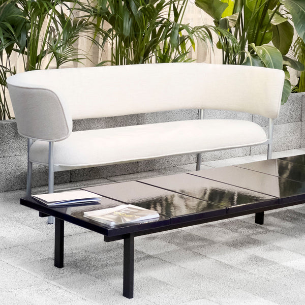 Elegant white curved sofa with light gray accents, paired with a sleek black coffee table in a modern outdoor setting.