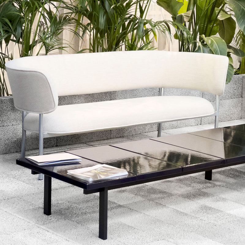 Elegant white curved sofa with light gray accents, paired with a sleek black coffee table in a modern outdoor setting.