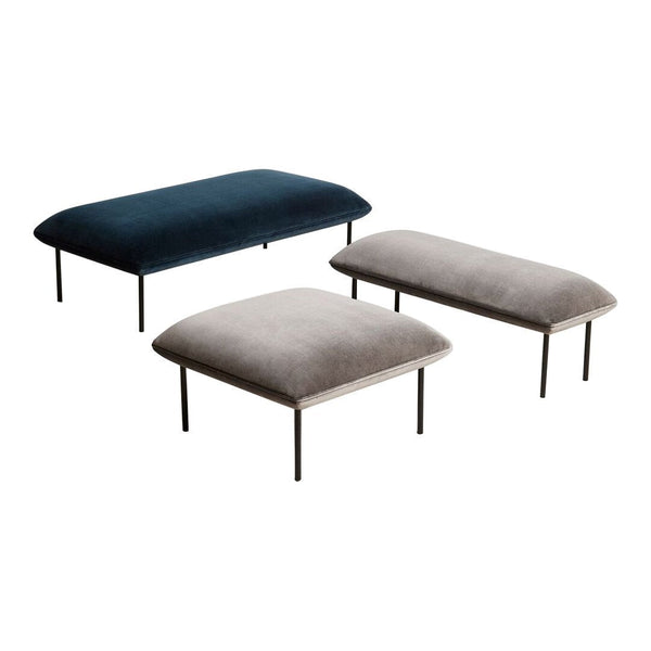 Three upholstered ottomans in dark blue and gray velvet, featuring smooth, clean lines and soft textures.
