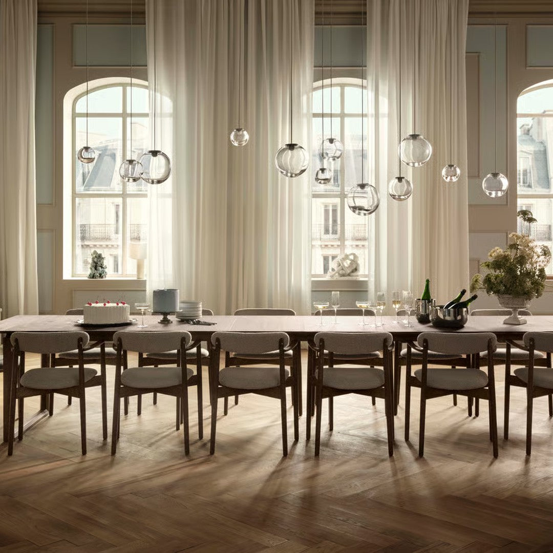 Elegant wooden dining table with light wood tones, paired with soft neutral curtains and decorative glass pendant lights.