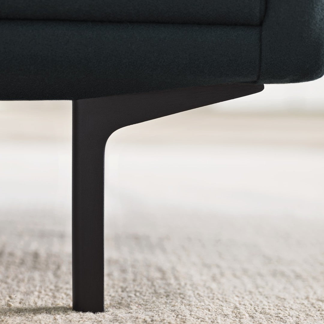 Dark green upholstered sofa with sleek black metal legs on a light carpet.
