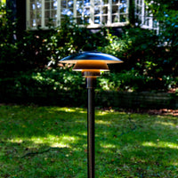 "Outdoor lamp with a sleek black pole and layered metallic shades in silver and gold tones, set against a green lawn."