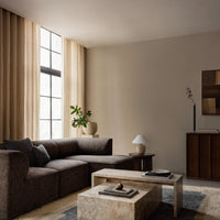 Earthy brown sofa with subtle textures, cream curtains, light beige walls, and a natural stone coffee table.