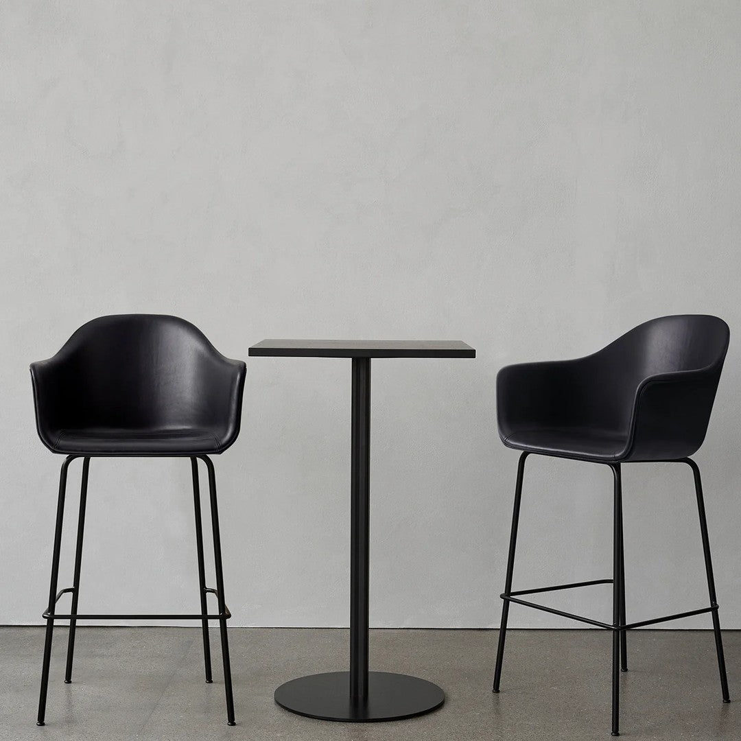 Modern black bar chairs and round table on a minimalist concrete background. Sleek, clean lines with a matte finish.