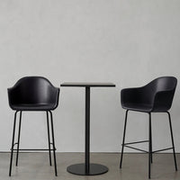 Modern black bar chairs and round table on a minimalist concrete background. Sleek, clean lines with a matte finish.