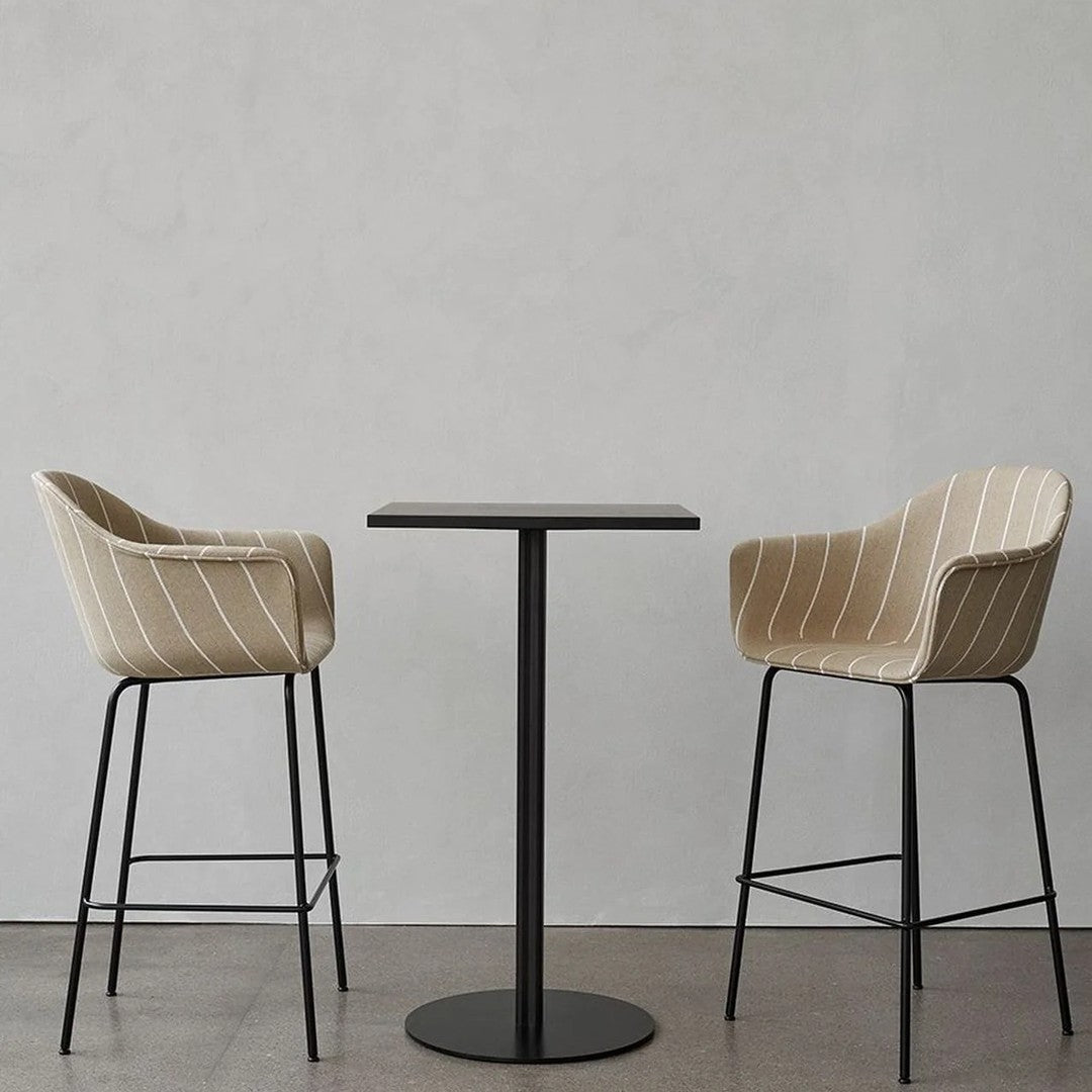 Beige striped upholstery on modern high chairs paired with a sleek black round table against a minimalist backdrop.