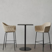 Beige striped upholstery on modern high chairs paired with a sleek black round table against a minimalist backdrop.