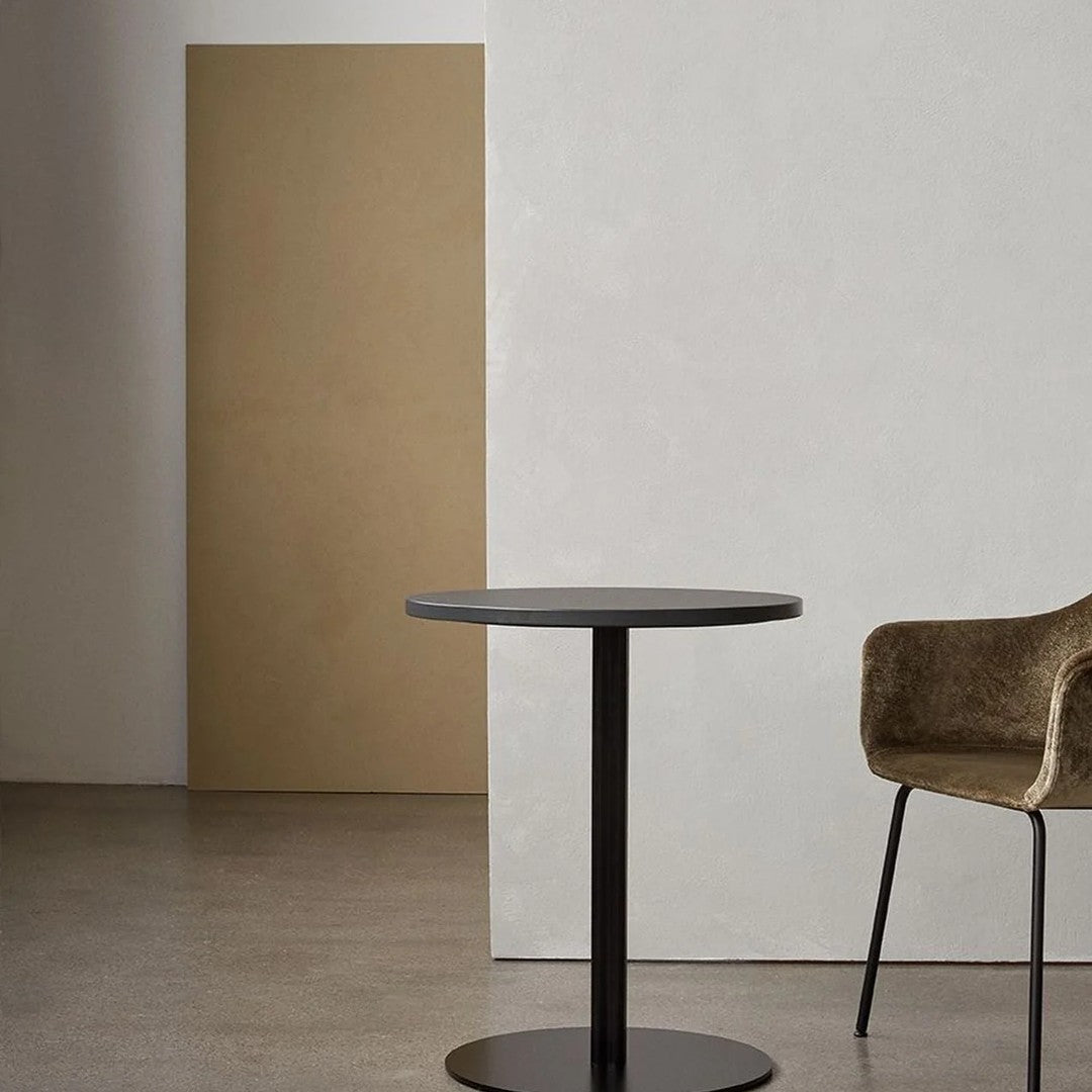 Black round table with a sleek finish and a warm beige background; soft-textured brown chair enhances the modern aesthetic.