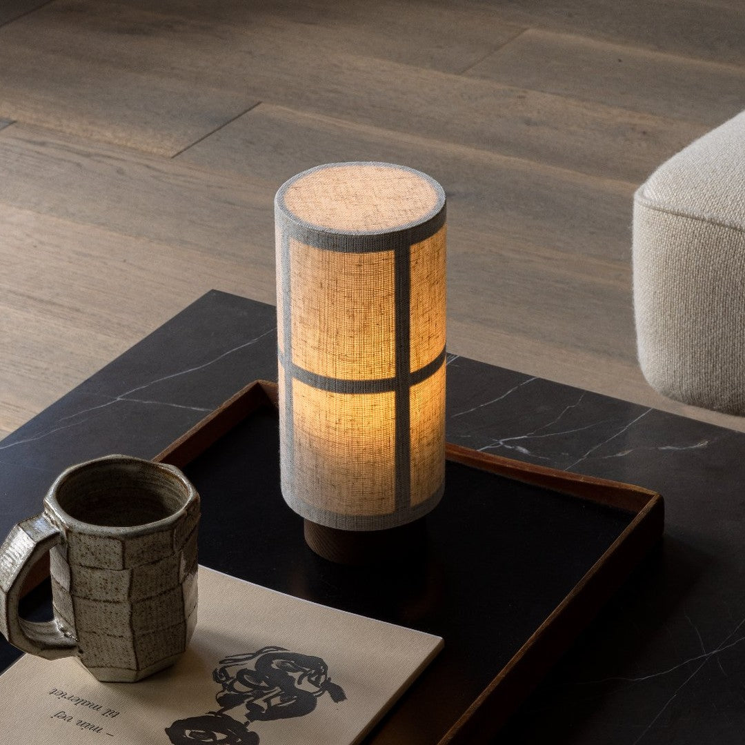 Modern cylindrical lamp with a textured white shade, featuring a warm amber glow and simple geometric patterns.