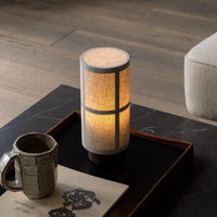 Modern cylindrical lamp with a textured white shade, featuring a warm amber glow and simple geometric patterns.