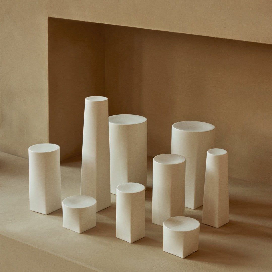 Assorted white ceramic vases with various geometric shapes against a neutral beige backdrop.