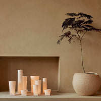 Various soft-hued candle holders in white and peach tones, set against a warm, beige background.