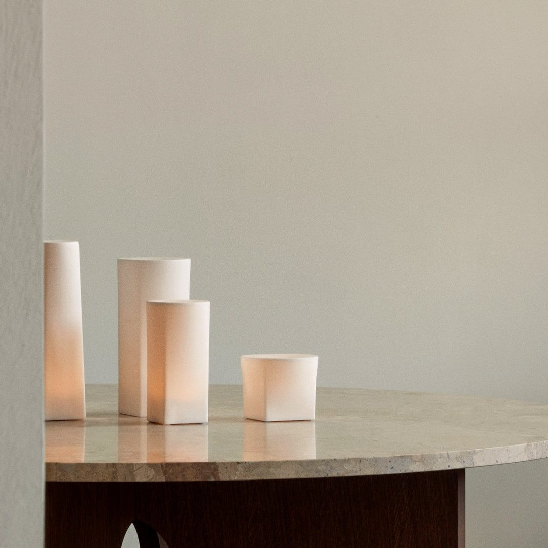 Soft white cylindrical lamps on a minimalist stone table, casting a warm glow against a neutral background.