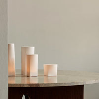 Soft white cylindrical lamps on a minimalist stone table, casting a warm glow against a neutral background.