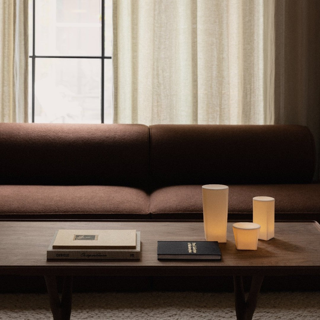 Brown textured sofa with white and amber accent candles, complemented by black and white books on a wooden table.