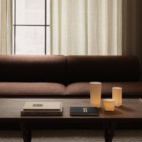 Brown textured sofa with white and amber accent candles, complemented by black and white books on a wooden table.