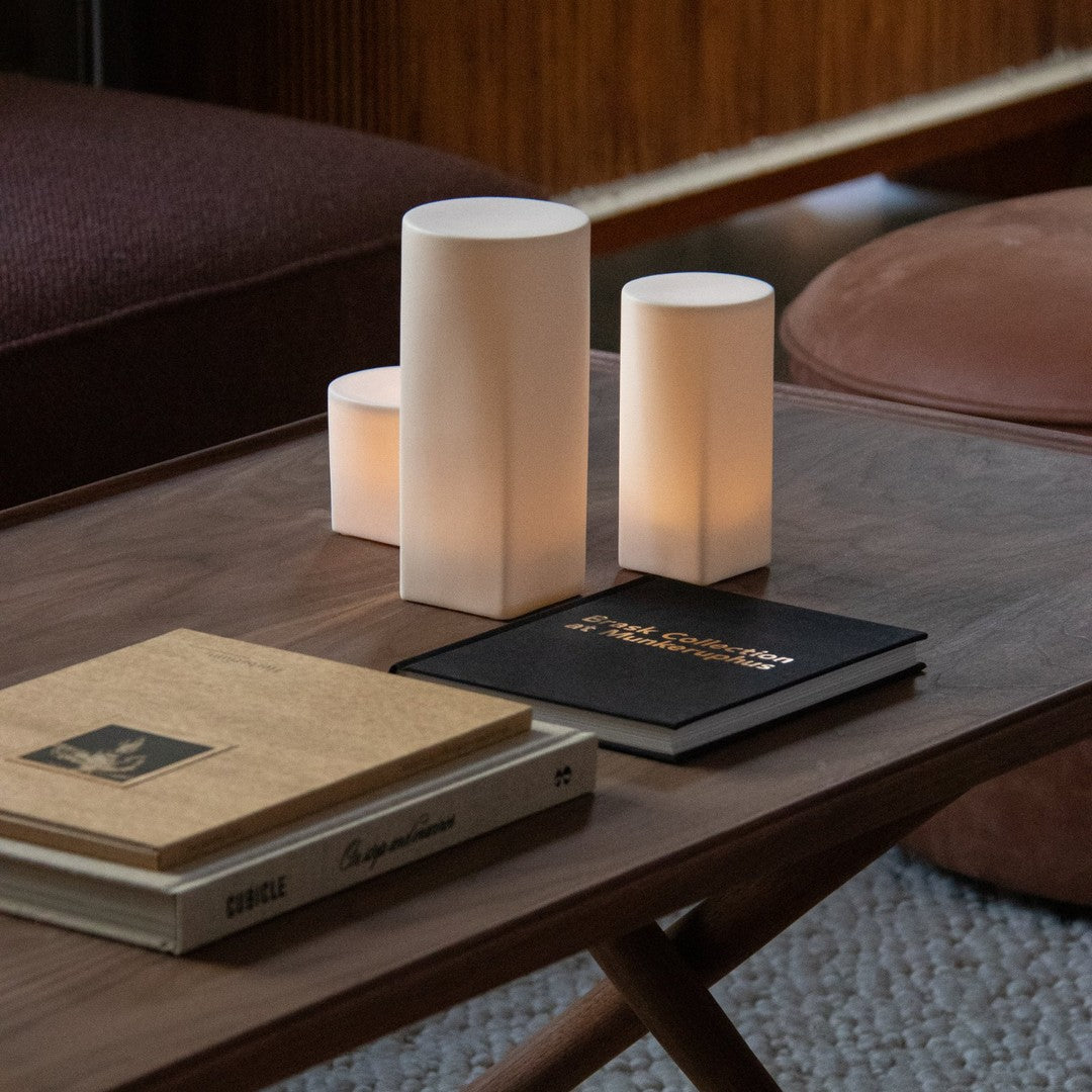 Soft white cylindrical lamps on a wooden table with beige and black books, creating a warm, cozy atmosphere.