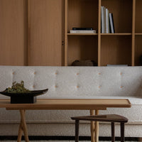 Beige textured sofa with button detailing, paired with a light wooden table and dark wood stool, set against a natural backdrop.