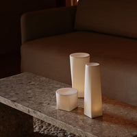 Modern geometric candles in varied heights, soft white color against a textured brown stone table.