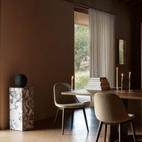 Neutral tones with soft beige chairs, dark accents, and a striking marbled pedestal create a warm, inviting ambiance.