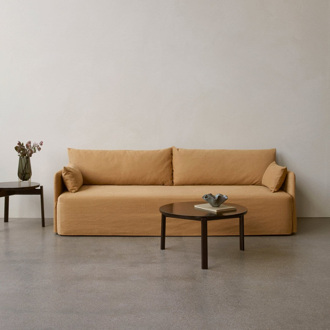 Mustard yellow sofa with two plush cushions, paired with a round wooden coffee table on a concrete floor.