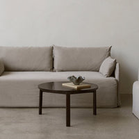 Beige sofa with soft cushions, paired with a dark wooden coffee table on a neutral-toned floor. Minimalist design.